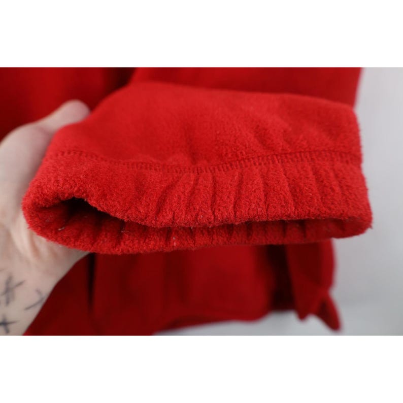 May include: Close-up of a bright red fleece jacket sleeve. The cuff is ribbed and the fabric has a soft, textured appearance. The sleeve is slightly bunched at the cuff.