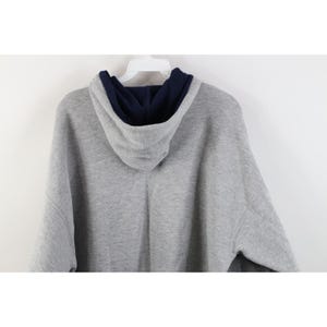 May include: A heather gray long-sleeve hooded sweatshirt featuring a contrasting dark navy blue interior lining within the hood. The garment is displayed on a white plastic hanger, showing the back view of the hood and the upper shoulder area.