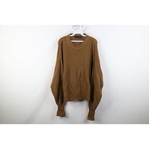 May include: A brown, long-sleeved sweater with a crew neck and ribbed cuffs. The sweater features a textured knit design and a logo on the chest. The sweater is hanging on a white hanger against a white background.