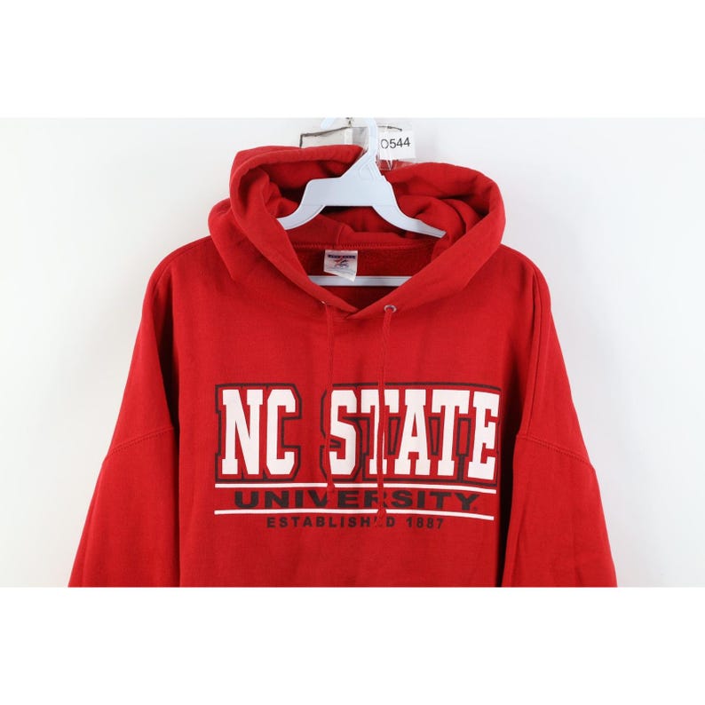 Peut inclure: Un sweat-shirt &agrave; capuche rouge avec le texte "NC STATE UNIVERSITY ESTABLISHED 1887" en lettres blanches. Le sweat-shirt a une capuche &agrave; cordon et une poche kangourou.