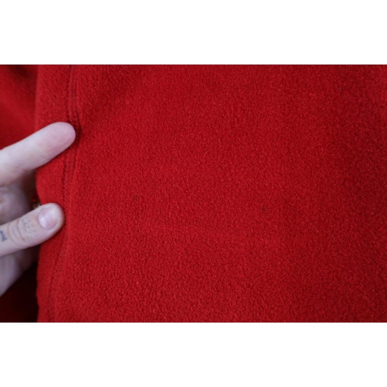 May include: Close-up of a vibrant red fabric with a textured surface. The fabric appears to be a soft material, possibly fleece or a similar textile. The image highlights the color and texture of the material.