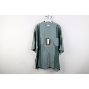 May include: A short-sleeved, button-down shirt in shades of teal and green, hanging on a white hanger. The shirt features a mandarin collar, a chest pocket, and mesh paneling on the sides. A tag is attached.