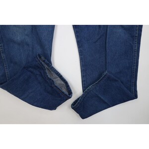 Op de afbeelding: Een paar blauwe denim jeans, plat op een witte ondergrond. De jeans hebben een medium wassing, zichtbare naden en een klassiek vijf-zakken ontwerp. De zomen zijn licht gerafeld, wat wijst op een vintage of gedragen uitstraling.