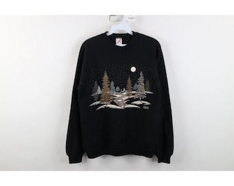May include: A black long-sleeve sweatshirt featuring a graphic print of a snowy forest landscape at night. The design includes various pine trees, a winding path, and a full moon set against a dark sky with white speckles representing stars.
