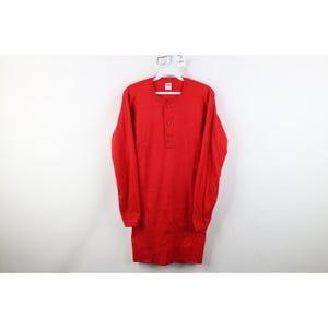 May include: A long-sleeved, red thermal shirt with a henley neckline and three buttons. The shirt is made of a ribbed knit fabric and hangs on a white hanger against a white background. The shirt has a classic, vintage style.
