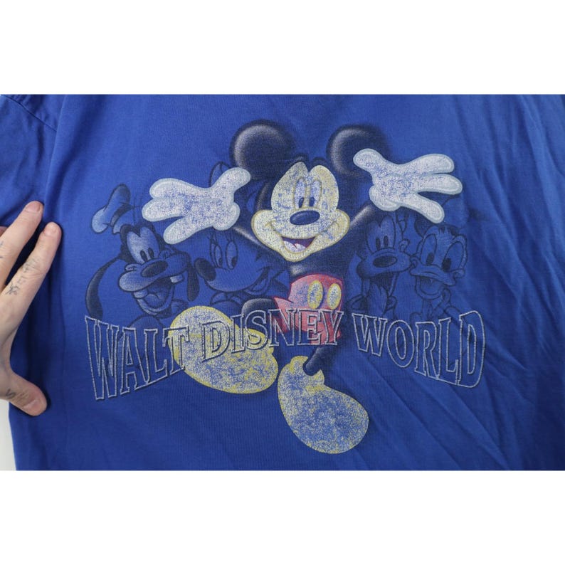 May include: Blue t-shirt featuring Mickey Mouse and friends with the text "Walt Disney World". The graphic includes Mickey Mouse, Goofy, Donald Duck, and other characters in a vintage style.