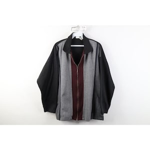 Puede incluir: Una chaqueta con cremallera completa que presenta un diseño de bloques de color con mangas negras, paneles laterales grises y una franja vertical central de color granate. La prenda incluye un cuello negro, una cremallera metálica plateada.