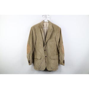 May include: A tan corduroy blazer with brown elbow patches, two front pockets, and dark brown buttons. The jacket is hanging on a white hanger against a white background. The blazer has a classic, tailored design.