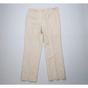 May include: Cream-colored, straight-leg pants with a classic design. The pants feature a button and zipper closure, belt loops, and front pleats. A tag is attached to the waistband. These pants are suitable for various occasions.