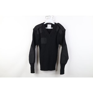 Może przedstawiać: Czarny sweter z dekoltem w serek z wzmocnionymi naszywkami na ramionach, łokciach i klatce piersiowej. Sweter jest prążkowany i ma długie rękawy z prążkowanymi mankietami. Wisi na białym wieszaku na białym tle.