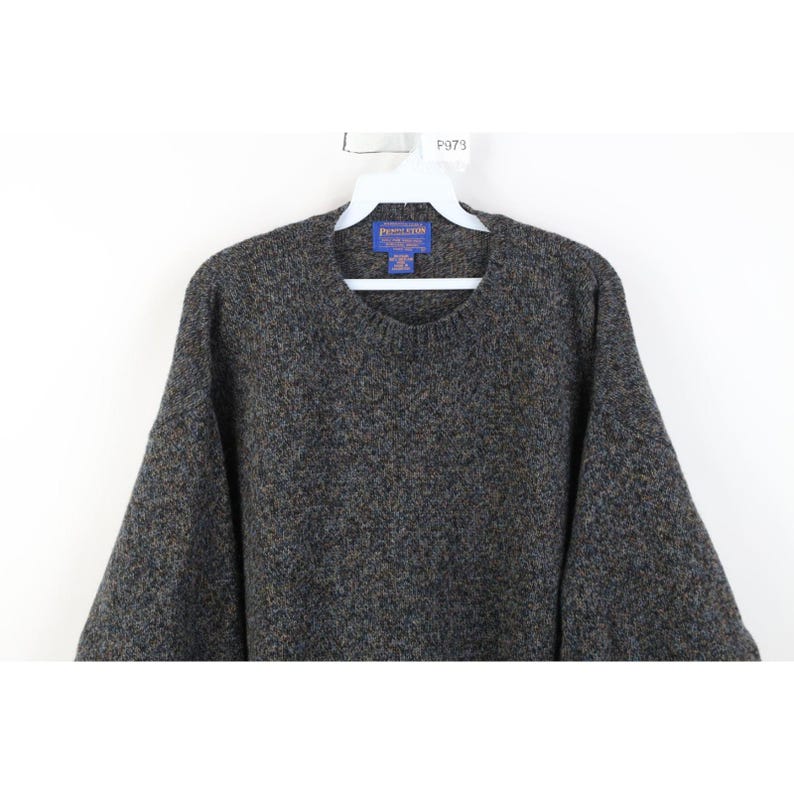 May include: A gray and brown speckled sweater with a crew neck, hanging on a white hanger. The sweater has a label that reads "Pendleton". The sweater is made of a thick, textured material.