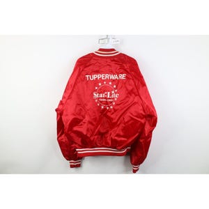 Könnte beinhalten: Rote Satinjacke mit weißem Besatz an Kragen, Manschetten und Bund. Die Jacke trägt den Schriftzug "Tupperware" über einem Sternmuster mit "Star-Lite Toledo Ohio" darunter.