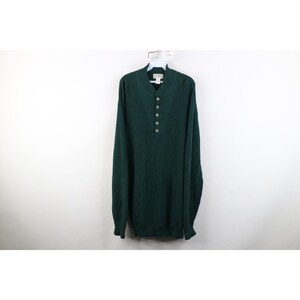May include: A dark forest green long-sleeve sweater featuring a mock neck collar and a partial button-down placket with five buttons. The knit garment includes a ribbed texture along the neckline and placket area, with a label at the collar.