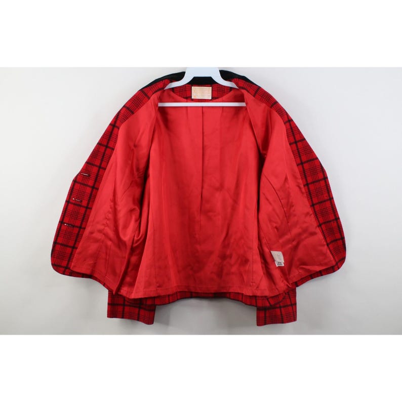 Peut inclure: Un blazer &agrave; carreaux rouges et noirs avec une doublure en satin rouge. Le blazer est ouvert, r&eacute;v&eacute;lant la doublure int&eacute;rieure et un col noir. Le v&ecirc;tement est suspendu &agrave; un cintre blanc sur fond blanc.
