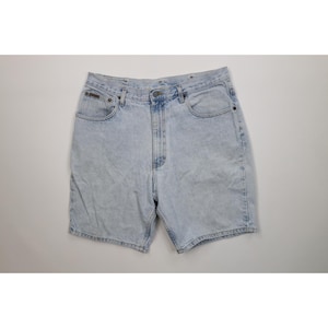 May include: Light blue denim shorts with a classic five-pocket design. The shorts have a button and zipper closure, belt loops, and a faded wash. The shorts are a casual style.