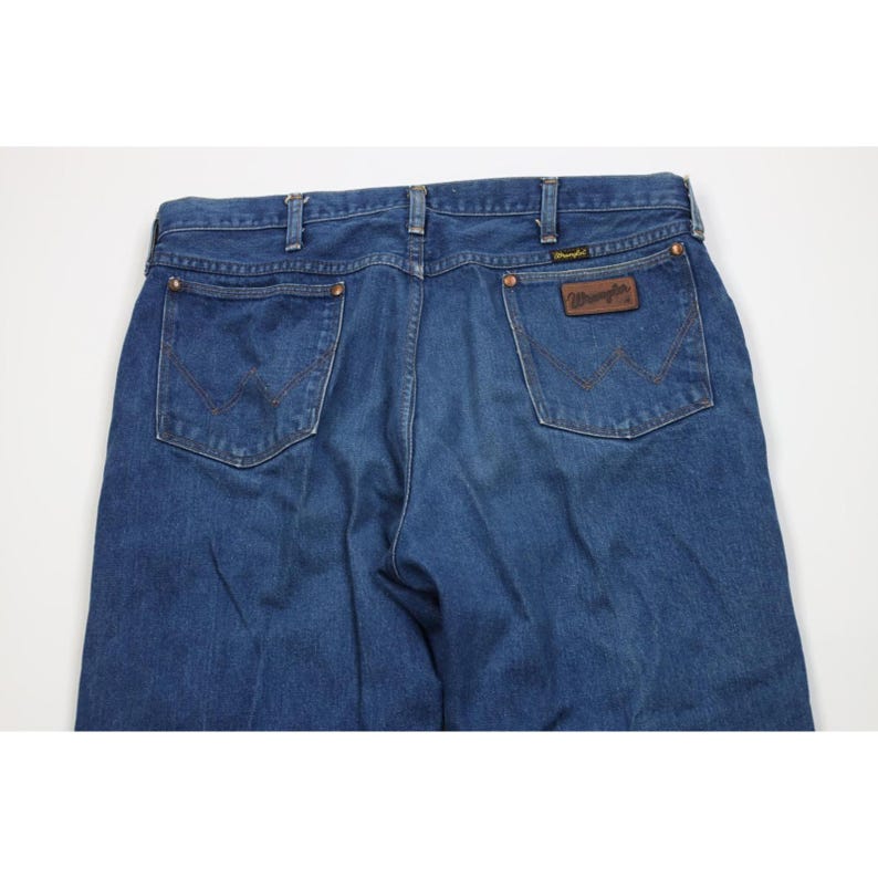 Op de afbeelding: Blauwe denim jeans met het Wrangler-logo op de achterzak. De jeans hebben een klassiek ontwerp met vijf zakken en een rechte pijp. De jeans zijn gemaakt van een duurzame denim stof.