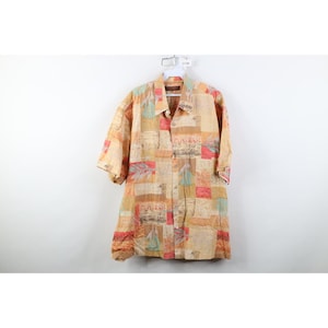 May include: A short-sleeved button-down shirt with a patchwork design in shades of tan, orange, and teal. The shirt features a collared neckline and is hanging on a white hanger against a white background. The fabric has a textured appearance.