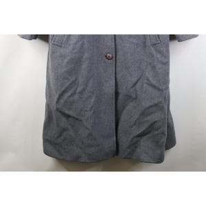 May include: A gray wool coat with a single brown button closure. The coat has a classic design with a notched collar and two front pockets. The sleeves are short, and the coat falls to mid-thigh length.