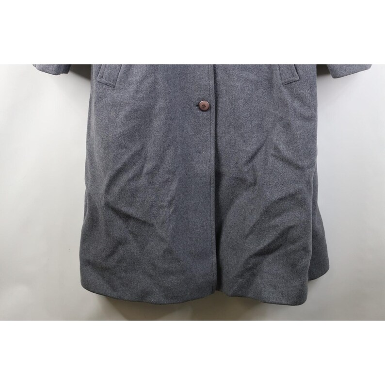 May include: A gray wool coat with a single brown button closure. The coat has a classic design with a notched collar and two front pockets. The sleeves are short, and the coat falls to mid-thigh length.