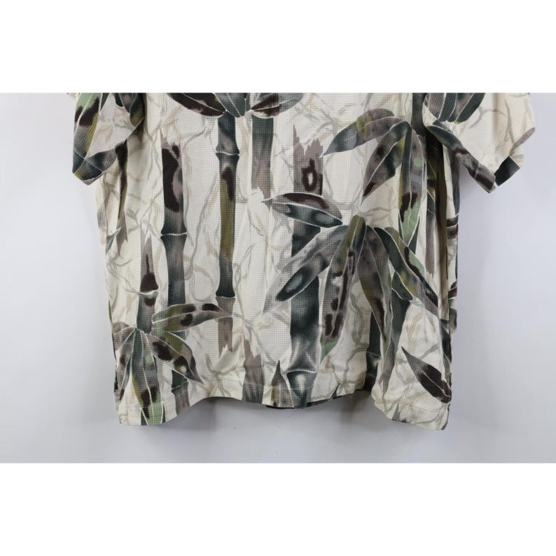 Op de afbeelding: Een shirt met korte mouwen met een bamboebladpatroon. Het shirt heeft een cr&egrave;mekleurige achtergrond met groene, bruine en grijze bamboestengels en bladeren. Het heeft een klassieke kraag en een relaxte pasvorm.