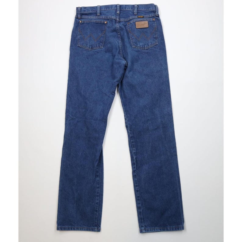 May include: Blue denim jeans with the Wrangler logo on the back pockets and a brown leather patch. The jeans have a classic five-pocket design and a straight leg cut.