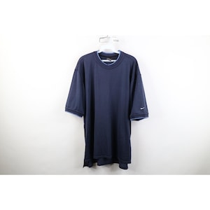 May include: A dark navy blue short-sleeve shirt featuring a light blue trim along the crew neckline and sleeve cuffs. The shirt has a small white Nike swoosh logo embroidered on the left sleeve and a straight hemline with side slits at the bottom.