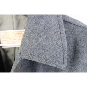 May include: Close-up of a gray wool coat collar. The coat has a classic design with a notched lapel. A tag with the brand name "Pendleton" is visible.