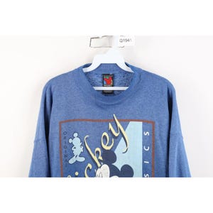 Op de afbeelding: Een blauwe gem&ecirc;leerde sweater met ronde hals en een grafische print met de tekst "Original Mickey Classics" en een silhouet van Mickey Mouse. Het kledingstuk heeft een geribbelde kraag en hangt aan een witte plastic hanger met een Q1941-label.