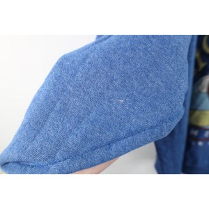 Op de afbeelding: Een blauw sweatshirt met lange mouwen en een gem&ecirc;leerde textuur. De stof is van middelzwaar gebreid materiaal. Aan de rechterkant is een deel van een grafische print zichtbaar, met gedempte tinten geel, groen en donkerblauw, met gedeeltelijke tekst.