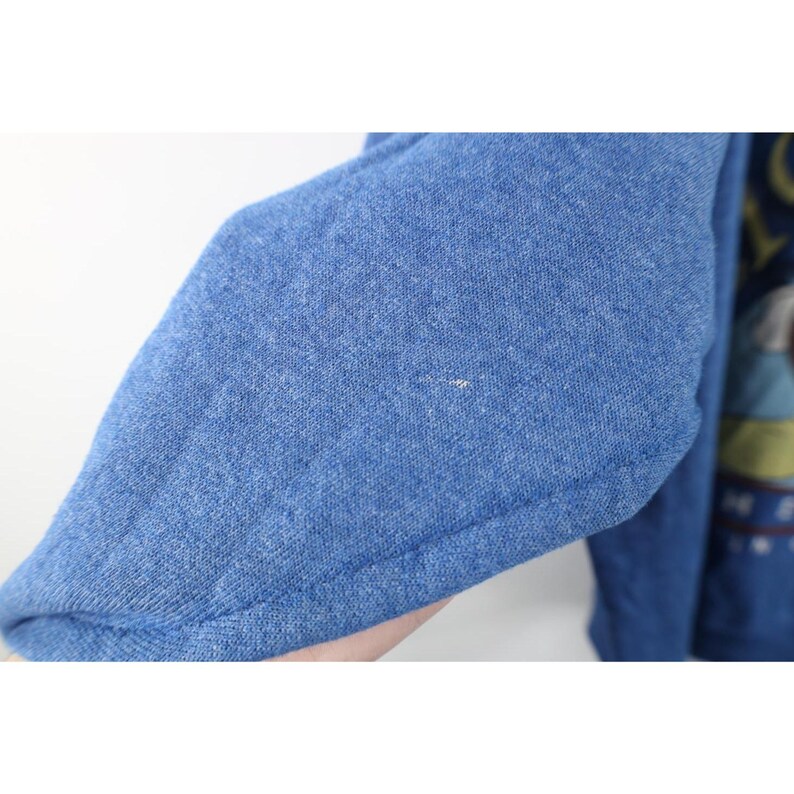 Op de afbeelding: Een blauw sweatshirt met lange mouwen en een gem&ecirc;leerde textuur. De stof is van middelzwaar gebreid materiaal. Aan de rechterkant is een deel van een grafische print zichtbaar, met gedempte tinten geel, groen en donkerblauw, met gedeeltelijke tekst.