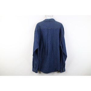 May include: A dark blue denim shirt with long sleeves, a button-down front, and a classic collar. The shirt has a relaxed fit and features contrasting orange stitching along the seams.