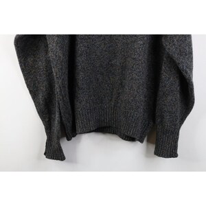 May include: A dark gray sweater with a ribbed hem and cuffs. The sweater has a speckled texture with hints of blue and brown. The sleeves are long and the overall style is casual and comfortable.