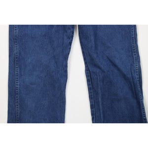 May include: Close-up of a pair of blue denim jeans. The jeans have a classic five-pocket design, with a straight leg cut. The denim has a medium wash, with subtle fading and wear. The seams are reinforced with sturdy stitching.