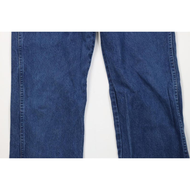 May include: Close-up of a pair of blue denim jeans. The jeans have a classic five-pocket design, with a straight leg cut. The denim has a medium wash, with subtle fading and wear. The seams are reinforced with sturdy stitching.