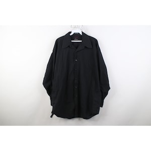 May include: A black button-down shirt with a wide collar, hanging on a white hanger. The long-sleeved shirt has a relaxed fit and is made of a solid black fabric. The shirt is unbuttoned at the top.