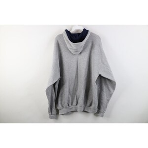 May include: A heather gray long-sleeve pullover hoodie featuring a contrasting dark navy blue interior lining within the hood. The garment is constructed with a standard drawstring-free hood, ribbed cuffs at the sleeves, and a ribbed hemline.