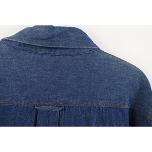 May include: Close-up of the back of a blue denim shirt. The collar and yoke are visible, with brown stitching. The fabric is a medium wash denim, and the shirt appears to be new or in excellent condition.