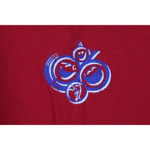 May include: A maroon-colored t-shirt featuring a distressed graphic design. The graphic is a series of connected, abstract shapes in blue and white. The design has a vintage, worn appearance.