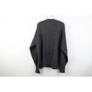 May include: A gray speckled sweater hanging on a white hanger. The sweater has long sleeves and a crew neck. The fabric appears to be a thick knit, suitable for cooler weather. The sweater is a neutral color, making it versatile for various outfits.