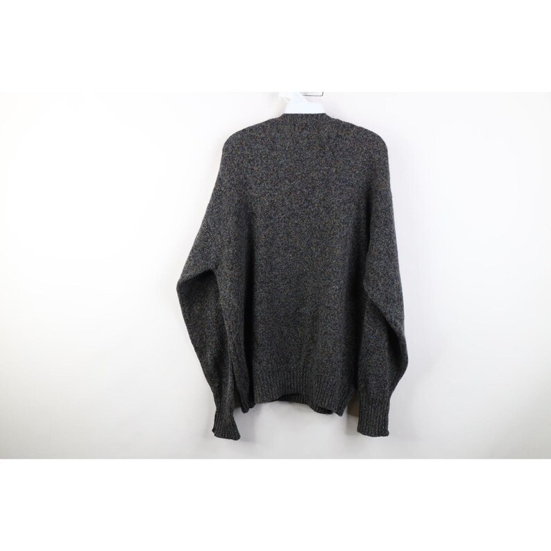 May include: A gray speckled sweater hanging on a white hanger. The sweater has long sleeves and a crew neck. The fabric appears to be a thick knit, suitable for cooler weather. The sweater is a neutral color, making it versatile for various outfits.