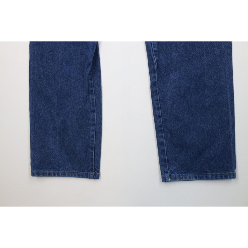 May include: Close-up of two legs of blue denim jeans. The jeans are a medium wash with visible texture and slight fading. The hems are straight and the fabric appears to be sturdy.