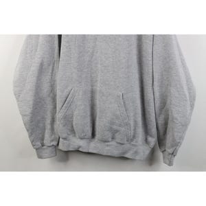 May include: A light gray long-sleeve pullover hoodie featuring a front kangaroo pocket, ribbed cuffs at the wrists, and a ribbed hemline. The garment is constructed from a heathered fabric with a consistent texture throughout the entire piece.