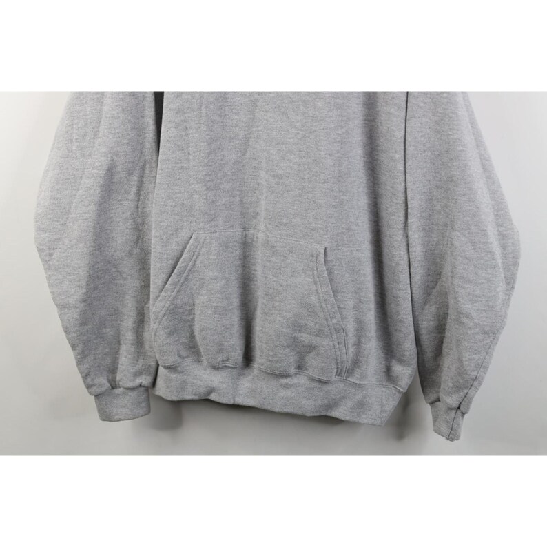 May include: A light gray long-sleeve pullover hoodie featuring a front kangaroo pocket, ribbed cuffs at the wrists, and a ribbed hemline. The garment is constructed from a heathered fabric with a consistent texture throughout the entire piece.