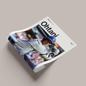 May include: A printed poster featuring a baseball player in a Dodgers uniform, mid-swing with a bat. The name "Ohtani" is printed in large black letters. The player is wearing a blue helmet with the Dodgers logo. The poster is on a light gray surface.