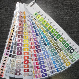 Peut inclure: Un éventail d'échantillons de couleurs avec un anneau métallique, présentant une large gamme de couleurs. Chaque carte présente plusieurs échantillons de couleurs avec des numéros correspondants. Les couleurs vont des pastels clairs aux teintes vives.