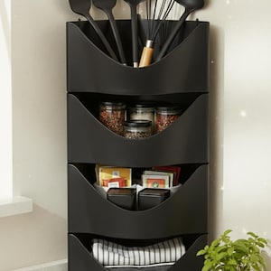 May include: A black kitchen storage unit with four sections. The top section holds cooking utensils, the second has spice jars, the third contains small containers and packets, and the bottom holds a folded tea towel.