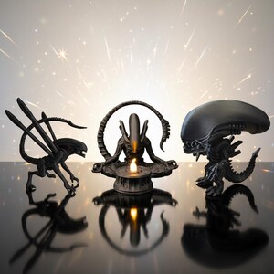 Puede incluir: Tres figuras negras de Alien se exhiben sobre una superficie reflectante. Las figuras incluyen un Alien de pie, un Alien en pose meditativa con una vela y un Alien con una cabeza grande. El fondo tiene efectos de luz brillantes.