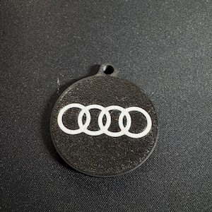 Può includere: Un portachiavi circolare nero con il logo Audi bianco. Il logo presenta quattro anelli intrecciati. Il portachiavi ha un piccolo foro nella parte superiore per l'attacco.