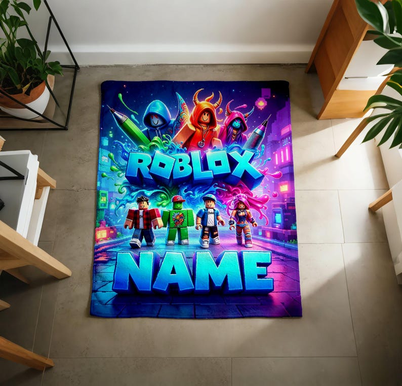 May include: A rectangular blanket featuring a vibrant Roblox-themed graphic with four blocky character figures, colorful paint splatters, and the text ROBLOX and NAME in large blue letters against a dark, neon-lit digital background.