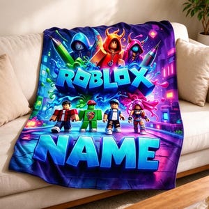 May include: A plush throw blanket featuring a vibrant Roblox graphic with characters, colorful paint splashes, and the text ROBLOX NAME in bold blue letters. The design includes a neon-colored city background with purple and blue tones.